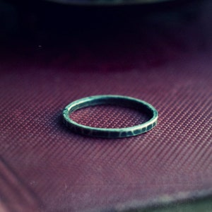 May include: A silver ring with a hammered texture sits on a burgundy leather-bound book.