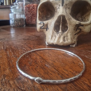 Peut inclure: Un bracelet jonc en argent avec une finition martelée. Le bracelet est ouvert et possède un fermoir simple et arrondi.
