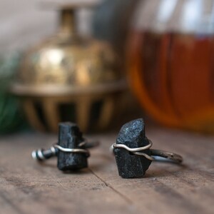 May include: Two black gemstone rings with silver wire wrapped around the stones. The rings are on a wooden surface.