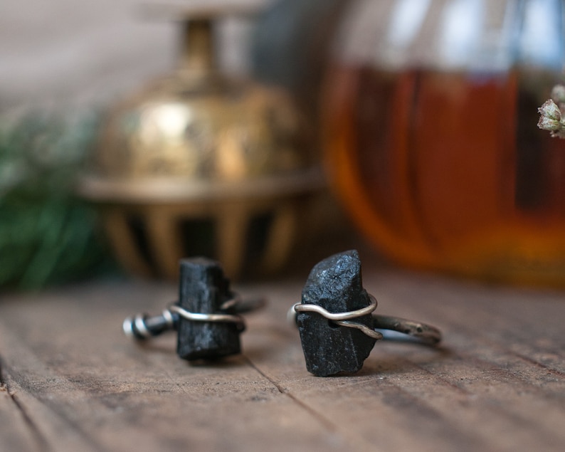 May include: Two black gemstone rings with silver wire wrapped around the stones. The rings are on a wooden surface.