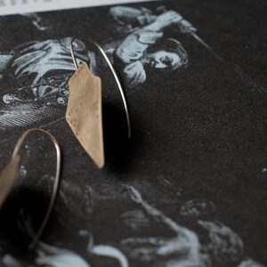 May include: A pair of silver earrings with a hammered, triangular shape. The earrings are hanging from a thin silver wire.