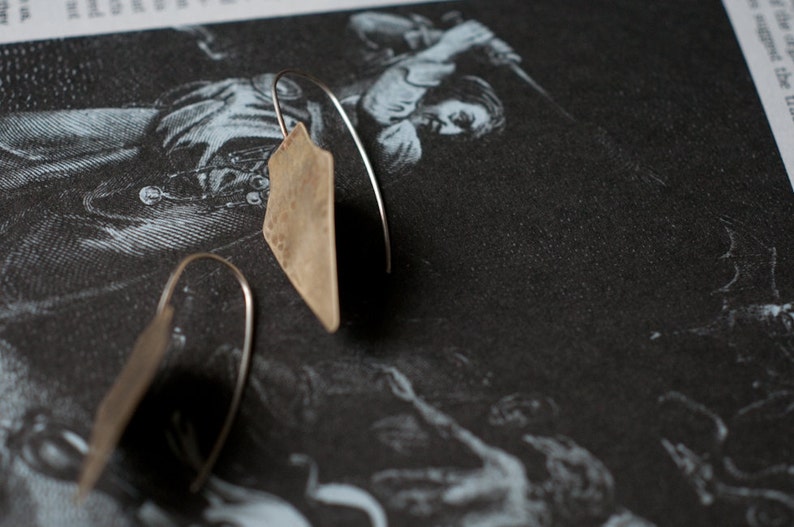 May include: A pair of silver earrings with a hammered, triangular shape. The earrings are hanging from a thin silver wire.