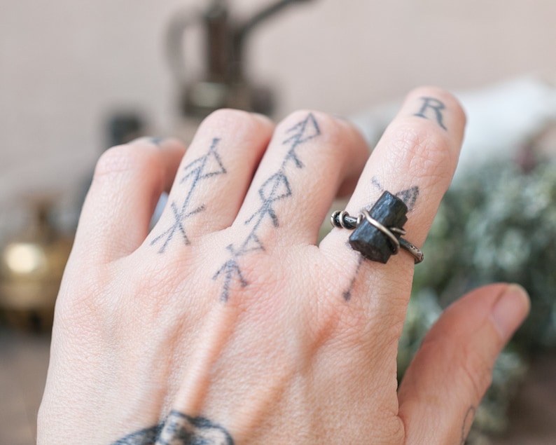 May include: A silver ring with a black tourmaline gemstone wrapped in wire. The ring is on a person's finger.