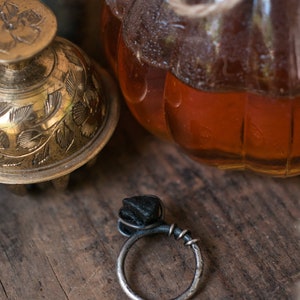 May include: A black stone ring with a silver band. The ring is set on a wooden surface.