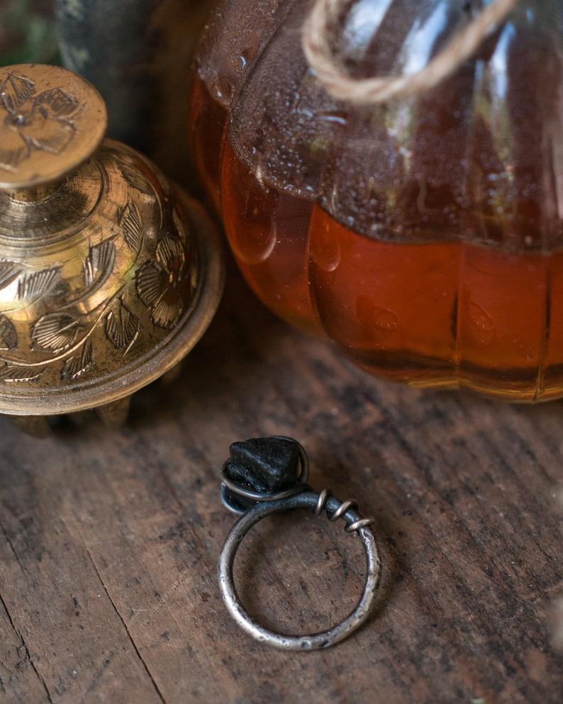 May include: A black stone ring with a silver band. The ring is set on a wooden surface.