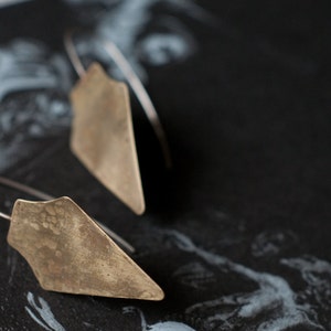May include: A pair of silver earrings with geometric, triangular shapes. The earrings are made of a textured metal and have a rustic, vintage look.