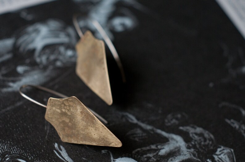 May include: A pair of silver earrings with geometric, triangular shapes. The earrings are made of a textured metal and have a rustic, vintage look.