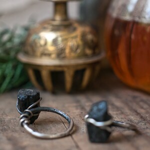May include: Two silver rings with black tourmaline stones. The rings are on a wooden surface.