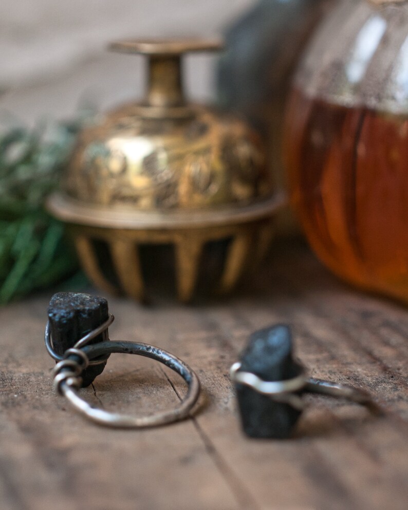 May include: Two silver rings with black tourmaline stones. The rings are on a wooden surface.