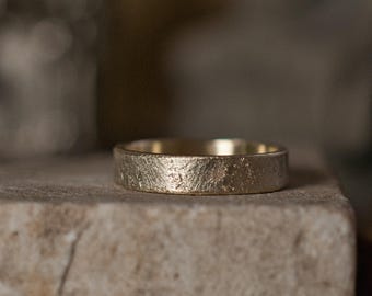 Rustieke gouden trouwring, 5 mm brede band gestructureerd tegen steen en genderneutraal voor hem, haar of zij.