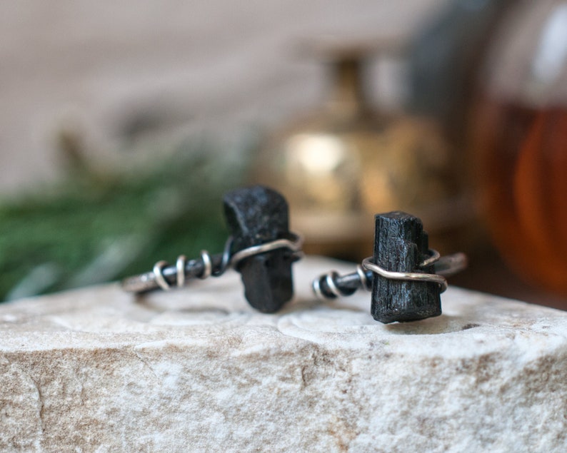May include: Two black tourmaline rings with silver wire wrapping. The rings are on a white stone surface.