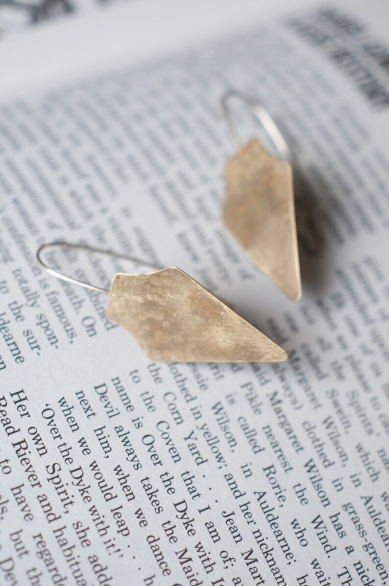 May include: A pair of silver earrings with a geometric, triangular shape. The earrings have a hammered, textured finish and a rustic, antique look.