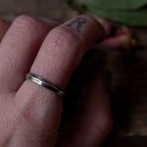 Puede incluir: Primer plano de un dedo con un anillo de banda plateado delgado.