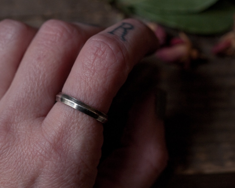 Puede incluir: Primer plano de un dedo con un anillo de banda plateado delgado.