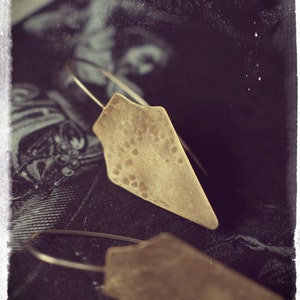 May include: A pair of gold-toned earrings with a hammered diamond shape. The earrings are hanging from a dark background.