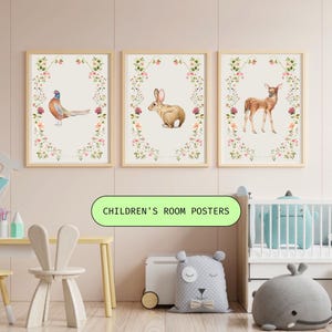 Può includere: Tre poster rettangolari da parete in cornici di legno chiaro, ognuno con un'illustrazione centrale di un animale—un fagiano, un coniglio e un cerbiatto—circondati da una delicata ghirlanda floreale di piccoli fiori rosa, gialli e verdi.