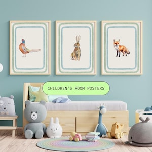 Op de afbeelding: Drie rechthoekige wandposters in lichte houten lijsten, elk met een aquarelillustratie van een bosdier: een fazant, een konijn en een vos. Elke poster heeft een crèmekleurige achtergrond met concentrische blauwe en groene lijnen.