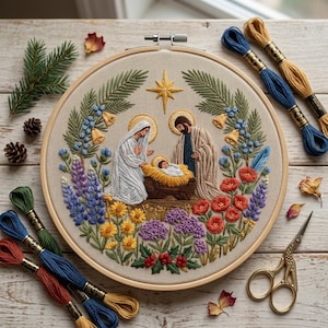 May include: A circular embroidery hoop featuring a nativity scene with Mary, Joseph, and the infant Jesus in a manger, surrounded by a wreath of embroidered flowers, pine branches, and a gold star, accompanied by embroidery floss and scissors.