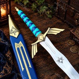 May include: A metal sword with a silver blade featuring a triangular emblem, a gold-coloured crossguard with wing-like extensions, and a handle wrapped in alternating blue and turquoise bands. It is accompanied by a blue scabbard with gold accents.