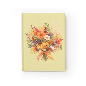 Può includere: Un taccuino con copertina rigida giallo pallido che presenta un'illustrazione centrale di un bouquet autunnale. La composizione include zucche arancioni, un gatto nero, un piccolo fantasma, foglie autunnali, bacche e fiori, legati da un nastro a quadri arancione.