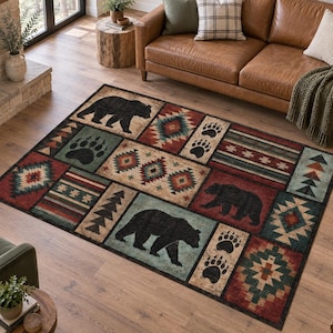 May include: A rectangular area rug featuring a patchwork design with black bear silhouettes, bear paw prints, and geometric patterns in shades of red, teal, tan, and brown. The rug is composed of multiple distinct panels arranged in a grid-like layout.