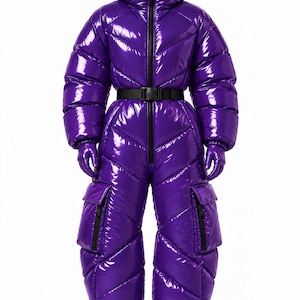 May include: A glossy purple puffer jumpsuit with a high collar, hood, and chevron-quilted pattern. It features a black front zip, a black buckled waist belt, two large cargo pockets on the thighs, and matching purple gloves. The text PuffHaus is visible.