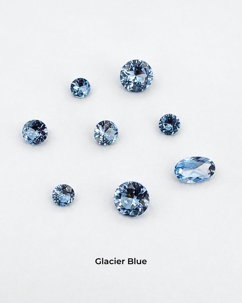 Eight faceted glacier blue stones on a pale grey background: three 2.5 mm rounds,
two 3 mm rounds, two 4 mm rounds and one 4 x 6 mm oval, shown loose so the
baby blue colour is visible. Labelled glacier blue.