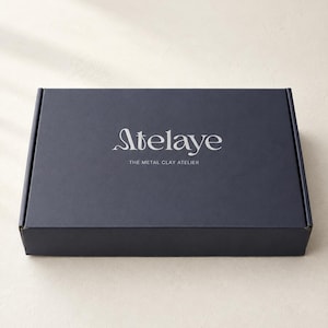 Closed silver clay kit tool box with Atelaye logo on a cream canvas roll, shown from above at desk height.