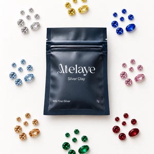 Pode incluir: Uma bolsa azul-escura com o rótulo Atelaye Silver Clay 999 Fine Silver 7g, rodeada por oito grupos circulares de pedras preciosas facetadas em várias cores, incluindo tons de amarelo, azul, rosa, vermelho, verde, azul-claro, transparente e âmbar.