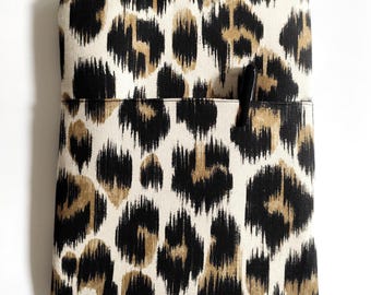 May include: A rectangular, zippered case with a black, tan, and white animal print. A black book with the text "Marguerite Duras ESCRIBIR" is partially visible. A black pen is in the front pocket.