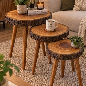 May include: A set of three nesting side tables featuring natural wood grain circular tops with rough, bark-covered edges and three tapered wooden legs each. The tables are arranged in a descending height order, showcasing a warm brown finish.