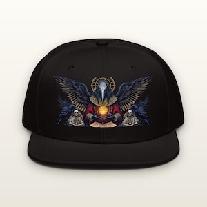 May include: A black baseball cap featuring a graphic print of a central figure with a bird-like mask, large wings, and a glowing orb. The design includes two ravens, two skeletal figures, and an open book, rendered in shades of red, gold, and blue.