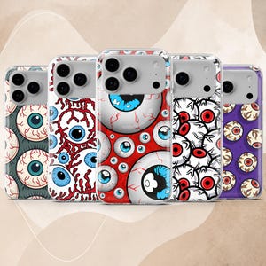 May include: Five clear phone cases featuring various graphic patterns of human eyeballs. The designs include blue and red irises on backgrounds of dark gray, white, red, and purple, with detailed red veins and black pupils visible on each case.