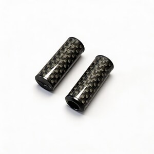 May include: Two cylindrical handle grips featuring a distinct black and grey woven carbon fiber pattern. Each grip has a smooth, solid black circular end cap and a hollow opening at the opposite end, presenting a sleek, uniform, and industrial appearance.