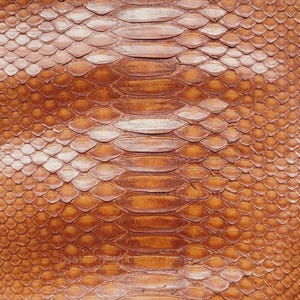 May include: A tan-colored snakeskin leather hide featuring a distinct pattern of overlapping scales and a central row of larger, elongated scales. The surface is embossed with the repeating text SIHANOUKVILLE TANNERY.