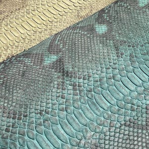 May include: Three pieces of textured snakeskin leather displayed in a diagonal arrangement. The top piece is light green, the middle is tan with brown markings, and the bottom piece is a vibrant teal with dark grey scale patterns.