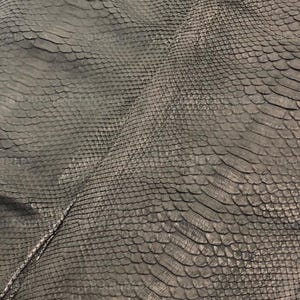 May include: A dark gray snakeskin leather hide featuring a distinct, repeating scale pattern across the entire surface. The texture is uniform with overlapping scales that create a tactile, layered appearance throughout the material.