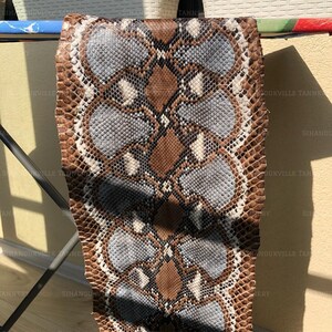 May include: A rectangular piece of snakeskin leather featuring a repeating diamond pattern in shades of brown, light blue, and white. The scales are small and textured, creating a distinct organic grid across the entire surface of the hide.