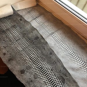 May include: Two long, rectangular pieces of textured snakeskin leather are displayed side by side. One piece features a high-contrast black and white scale pattern, while the other displays a uniform light gray scale texture throughout its length.
