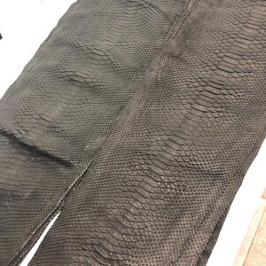 May include: A dark charcoal gray snakeskin leather hide featuring a distinct, repeating scale pattern across the entire surface. The material displays a textured, overlapping arrangement of individual scales that create a tactile, organic appearance.