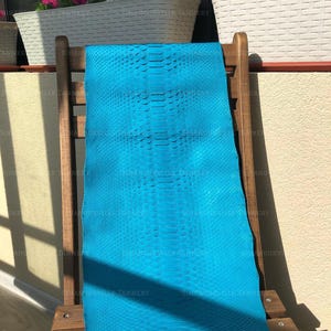 May include: A vibrant turquoise blue snakeskin hide featuring a distinct, symmetrical scale pattern running down the center. The leather has a smooth, uniform texture with a consistent bright color throughout the entire length of the material.