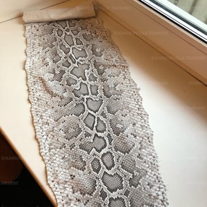 May include: A long, rectangular piece of natural snakeskin leather featuring a repeating diamond-shaped scale pattern in shades of grey, white, and black. The hide has a textured surface with visible individual scales and a rolled top edge.