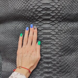 Puede incluir: Una pieza grande de piel de serpiente negra que presenta un patrón de escamas simétrico y distintivo con un acabado mate texturizado. El material muestra un diseño orgánico natural y repetitivo en toda su superficie detallada.