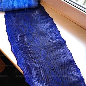 Può includere: Una pelle di serpente in cuoio blu reale vibrante caratterizzata da un distinto motivo a scaglie naturale con accenti blu scuro e neri su tutta la superficie. Il materiale è arrotolato nella parte superiore e presenta una finitura rettiliana.
