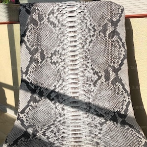 May include: A large, flat piece of snakeskin leather featuring a natural scale pattern in shades of grey, white, and black. The hide displays a prominent central spine with symmetrical diamond-shaped markings extending outward across the surface.