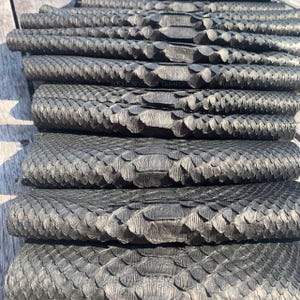 May include: A stack of dark charcoal gray snake skin leather hides with a distinct, overlapping scale pattern. Each hide features a textured surface with visible natural markings. The text SIBANOUVILLE TANNERY is printed on the leather.