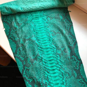 May include: A flat, rectangular piece of emerald green snakeskin leather featuring a distinct, dark-toned scale pattern running down the center. The surface displays a natural, textured reptilian hide with a vibrant, saturated green finish throughout.