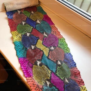 May include: A long, rectangular strip of snakeskin leather featuring a vibrant, multi-colored pattern of interlocking shapes in shades of magenta, lime green, royal blue, yellow, and deep red, with a distinct textured scale surface throughout.