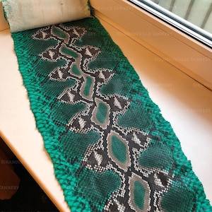 May include: A rectangular piece of emerald green and black snakeskin leather featuring a repeating diamond pattern with grey accents. The material has a textured, scaled surface and is laid out flat, displaying a natural organic hide shape.