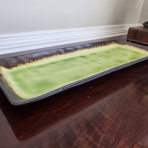 May include: A rectangular ceramic serving tray featuring a bright lime green center that transitions into a dark, textured brown border along the edges. The tray has a slightly raised rim and a smooth, glossy finish across the surface.